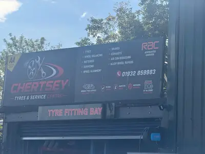 Chertsey Tyres & Service Centre sign above the tyre fitting bay listing tyres, wheel balancing, batteries, servicing, wheel alignment, brakes, exhausts, air con regassing and alloy wheel repairs, with the phone number 01932 859983